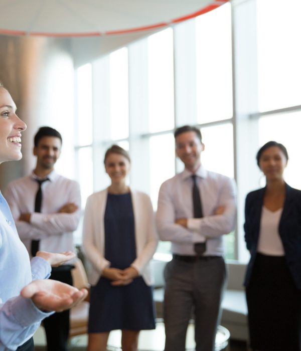 Portrait of successful female executive manager with open hands gesture standing in front of her team in office hall and announce good news